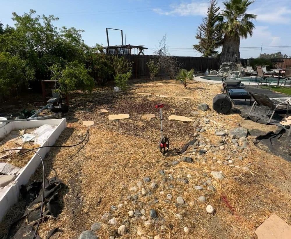 Dry backyard landscape with gravel, stones, pathways, and a pool area partially visible.